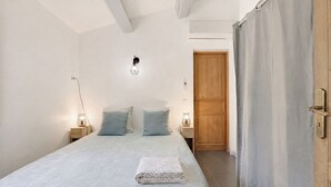 A bedroom with a bed, two bedside lamps, a wooden door, and a light switch on the wall. - Air-conditioned flat for 4 people with garden - Golfe de St-Tropez (Le Plan-de-la-Tour)