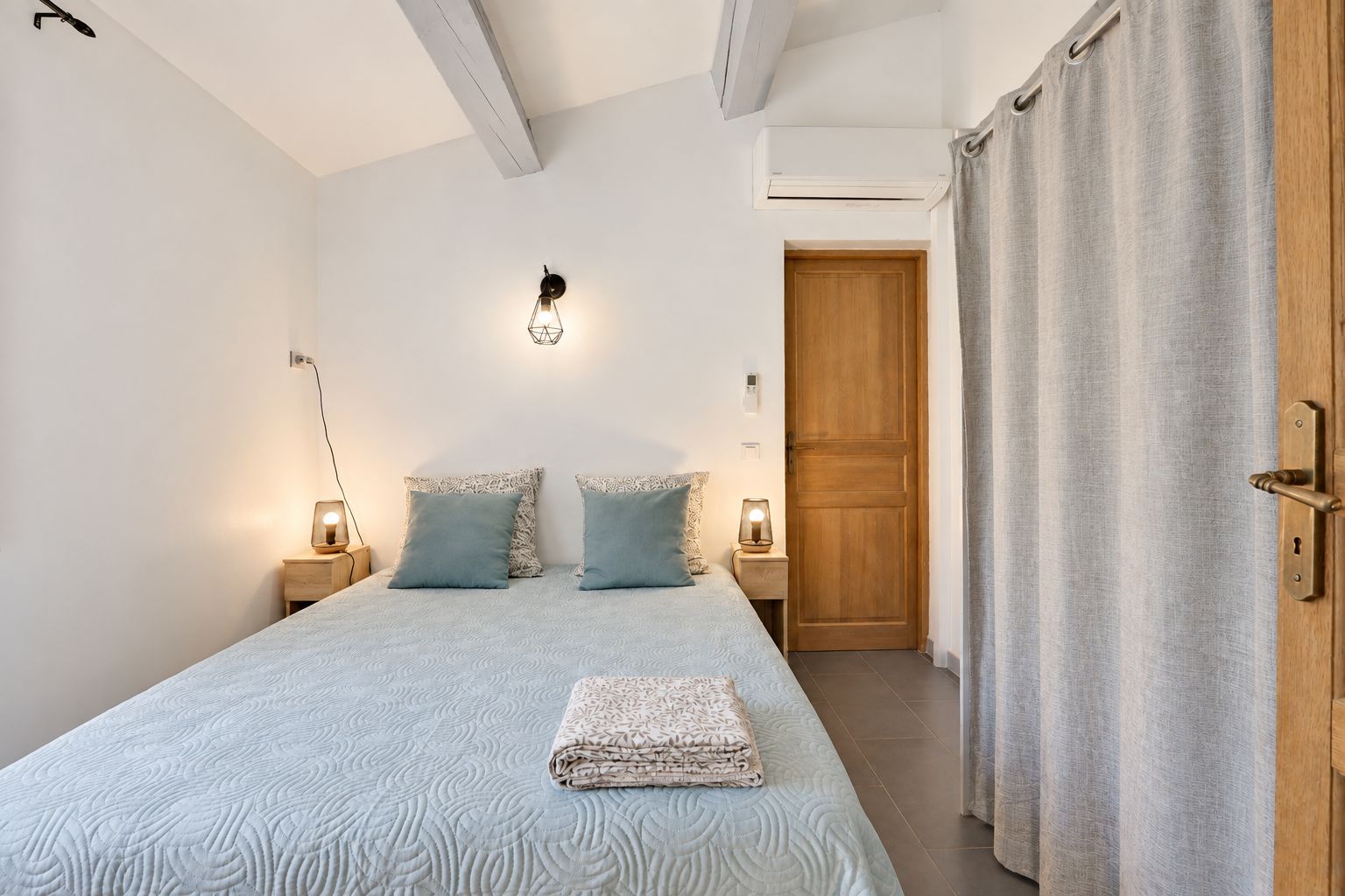Une chambre à coucher avec un lit, deux lampes de chevet, une porte en bois et un rideau.