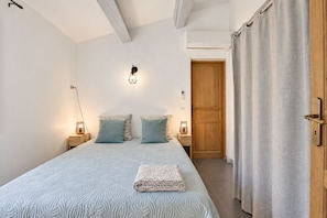 A bedroom with a bed, two bedside lamps, a wooden door, and a curtain.