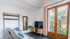 A living room with a sofa, a television, a wooden cabinet, and a large sliding glass door leading to a garden. - Air-conditioned flat for 4 people with garden - Golfe de St-Tropez (Le Plan-de-la-Tour)
