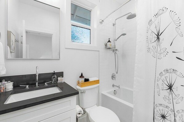 A bathroom with a white sink, a mirror, a shower, and a toilet. - The Greenwood Gem, Seattle (Seattle)