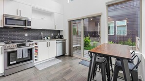 Une cuisine moderne avec des armoires blanches, un four à micro-ondes encastré et une cuisinière. On y trouve également un coin repas avec une table en bois et des chaises noires.
