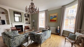 A spacious living room with a fireplace, a chandelier, and a large window with curtains.