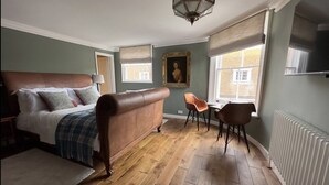A bedroom with a large bed, a wooden floor, a radiator, and a window with a view.