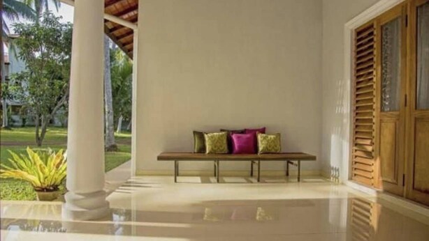 A clean, modern room with a bench against a wall, a large window with wooden shutters, and a view of a garden. - Coco Villa Peach Tree (Seeduwa - Katunayake)