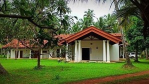 A bungalow with a red roof, surrounded by lush greenery and palm trees. - Coco Villa Peach Tree (Seeduwa - Katunayake)