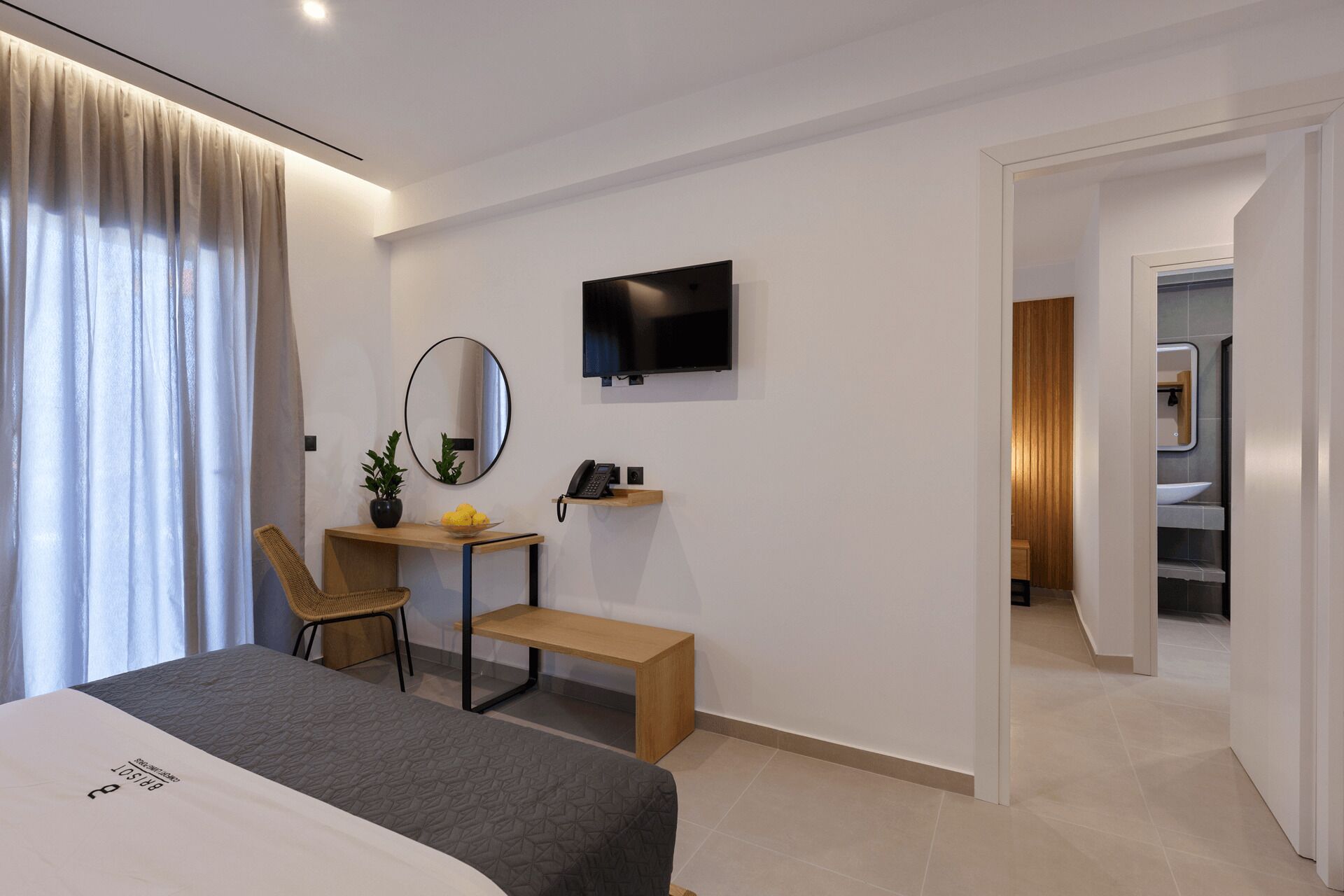 Une chambre d’hôtel moderne équipée d’un lit, d’un bureau avec une chaise, d’une télévision, d’un miroir et d’une petite plante.