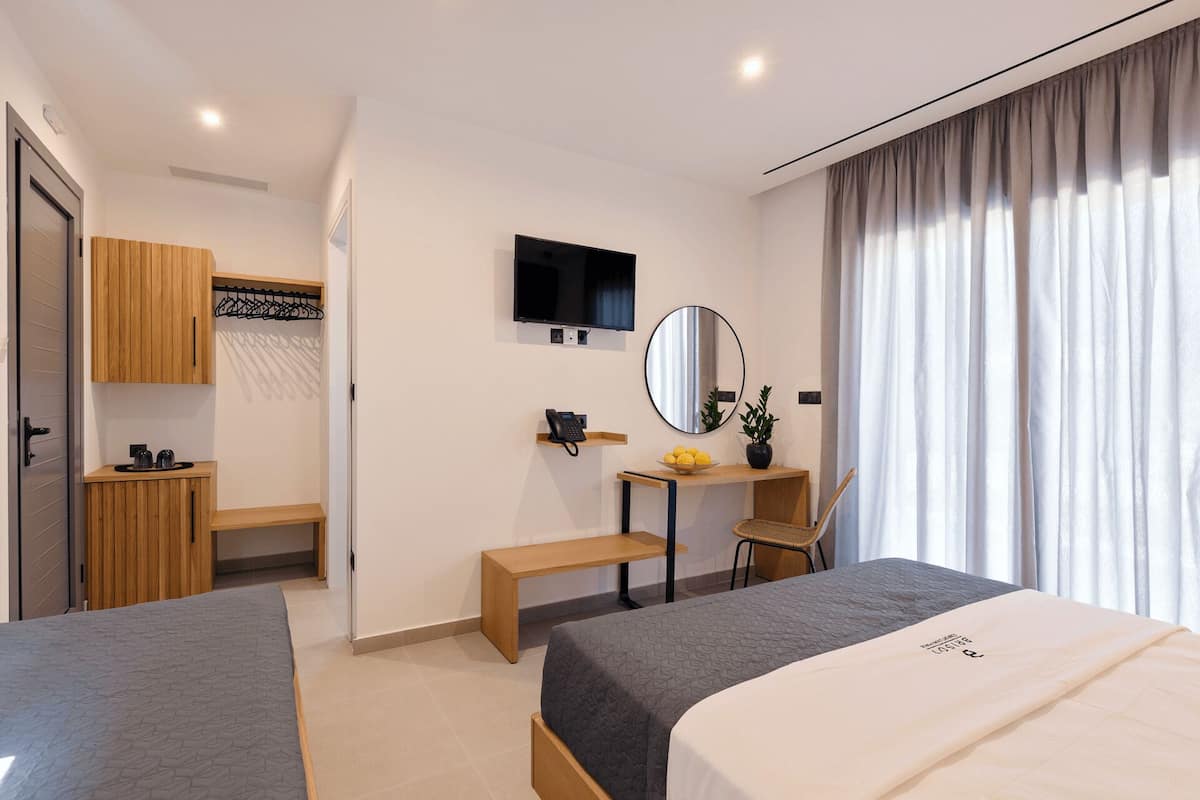 A modern hotel room with two beds, a desk, a chair, a TV, a mirror, and a window with curtains.