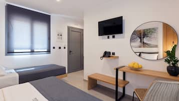 A modern hotel room with a bed, a desk with a chair, a TV, a mirror, and a window with blinds.