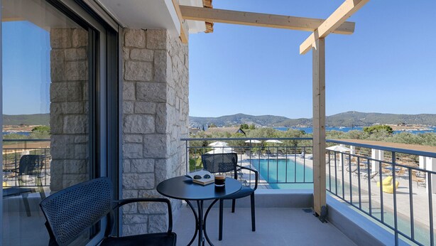 Un balcón con pared de piedra, piscina y vista al mar y las colinas.
