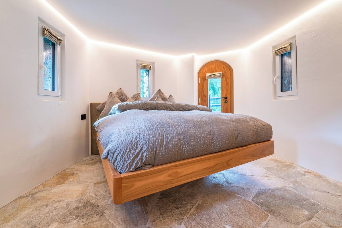 Ein Schlafzimmer mit einer hängenden Bett, Steinböden und zwei mit Vorhängen versehenen Fenstern.