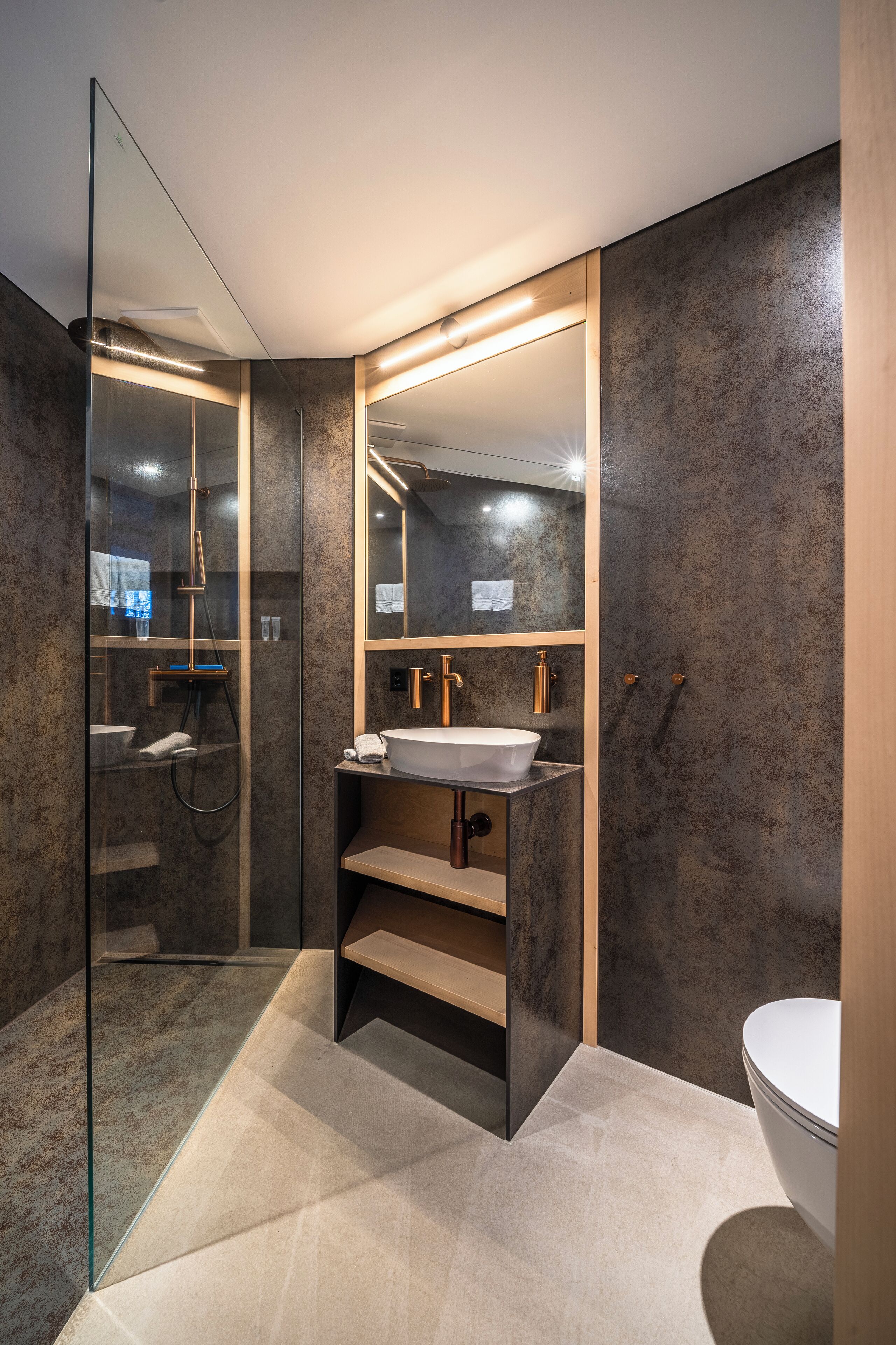 Une salle de bain moderne avec une douche à parois de verre, un lavabo blanc doté de robinetterie dorée et un grand miroir.