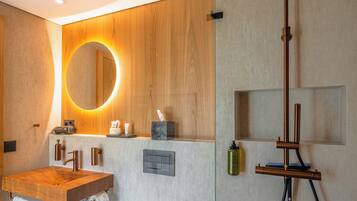 A modern bathroom with a wooden vanity, a round mirror, a toilet, and a shower with a unique headrest.