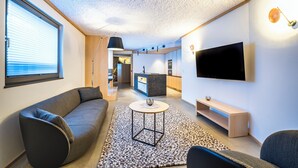 Una sala de estar moderna con un sofá, una mesa de centro, un televisor y una cocina al fondo.