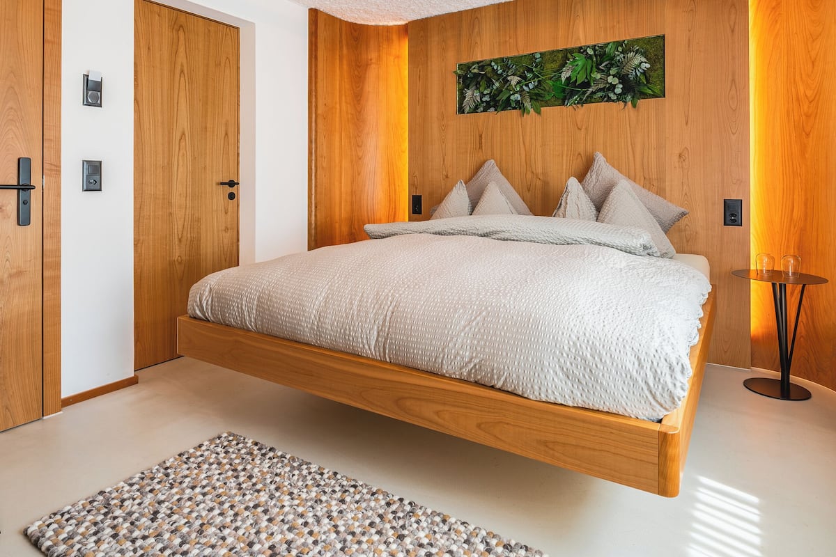 Ein modernes Schlafzimmer mit einem schwebenden Bett, Holzpaneelwänden, einer strukturierten Decke und einem gemusterten Teppich.