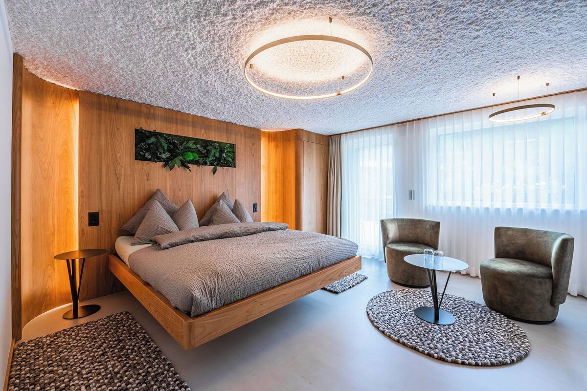 Ein modernes Schlafzimmer mit einem schwebenden Bett, einem runden Tisch, zwei Sesseln und einem großen Fenster mit transparenten Vorhängen.