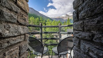 Ein Balkon mit zwei Stühlen, einer Steinmauer und Blick auf Berge und Bäume.