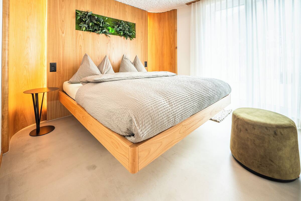 Ein modernes Schlafzimmer mit einem Holzbett, einem kleinen runden Hocker und einer wandmontierten Pflanze.