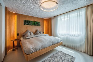 Un dormitorio moderno con una cama flotante, paneles de madera, una lámpara redonda y cortinas de gasa.