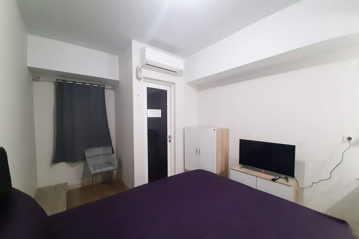 A bedroom with a bed, a TV, a wardrobe, and an air conditioning unit.