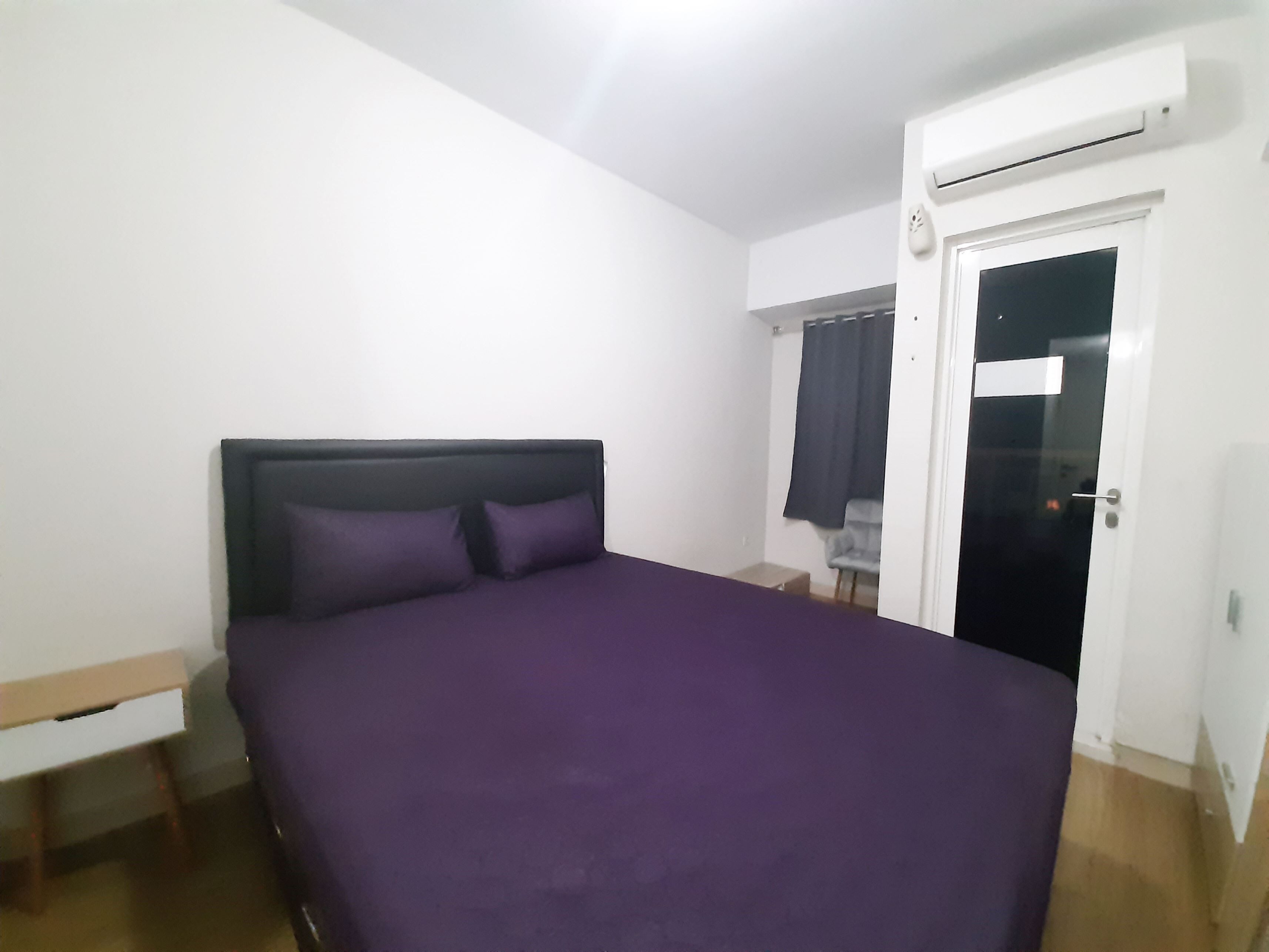 A bedroom with a bed, a nightstand, a chair, and an air conditioning unit.
