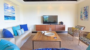 A living room with a sofa, a coffee table, a TV, and a wicker chair. - Premium Four Bedroom Condo (Punta de Mita)