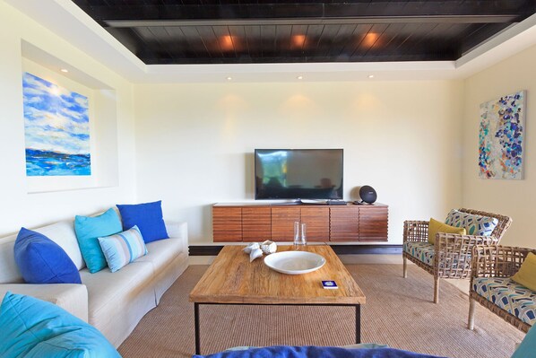 A living room with a sofa, a coffee table, a TV, and a wicker chair.
