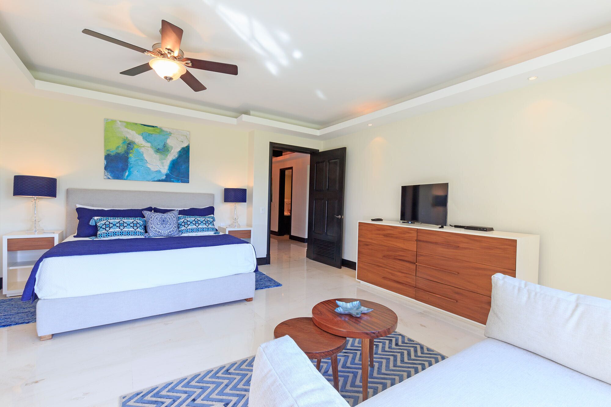 Une chambre à coucher moderne avec un lit, un ventilateur de plafond, une télévision et une commode.