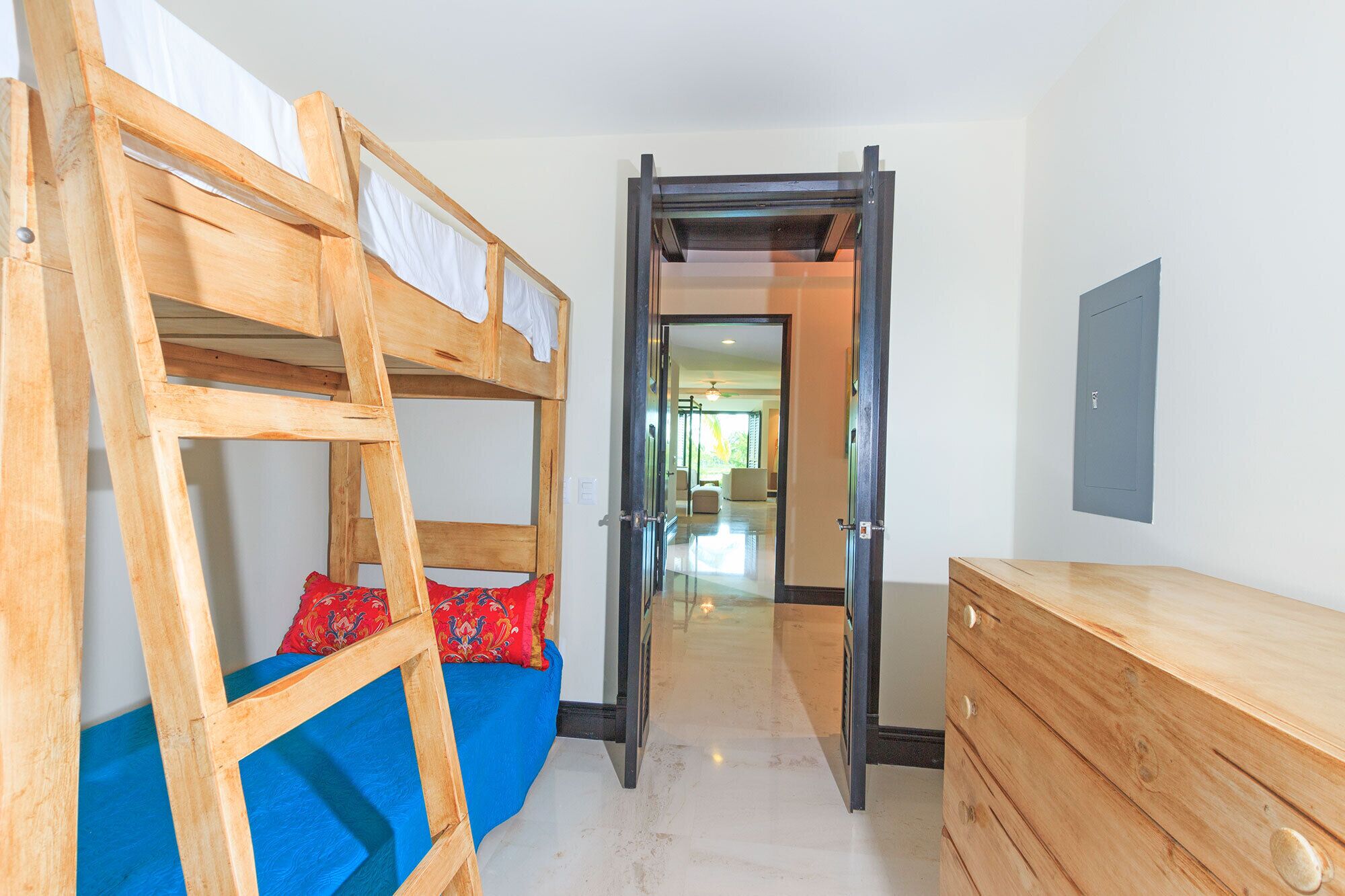 Una habitación con una cama litera, un escritorio y una puerta que da a otra estancia.