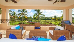 A covered outdoor seating area with wicker furniture, ceiling fans, and a view of a golf course. - Premium Four Bedroom Condo (Punta de Mita)