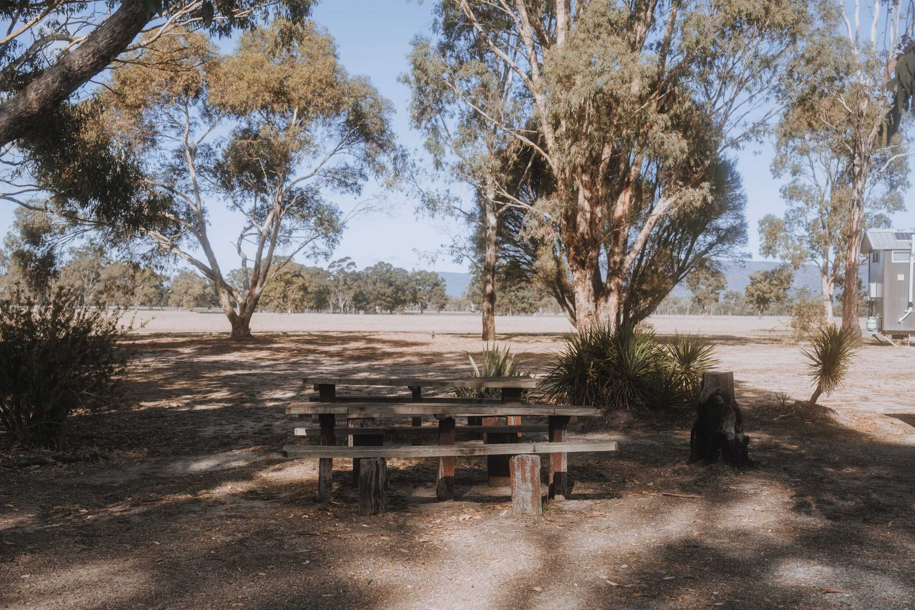 Una mesa de picnic en un parque con árboles y un edificio al fondo.