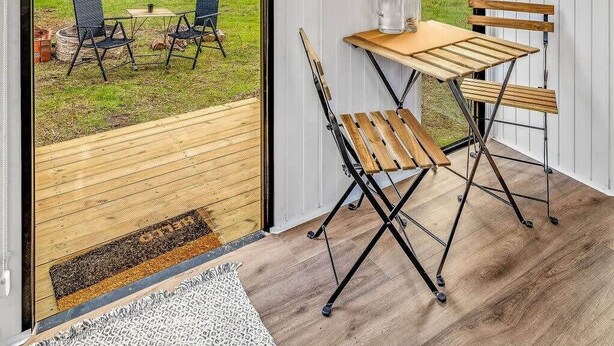 Una habitación moderna con ventanas amplias, una mesa de madera con sillas y vistas a un espacio exterior con césped.