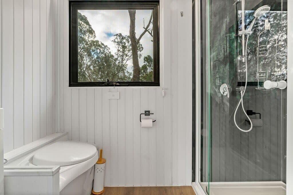 A bathroom with a toilet, a window with a view of trees, and a glass-enclosed shower area.