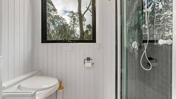 A bathroom with a toilet, a window with a view of trees, and a glass-enclosed shower area.