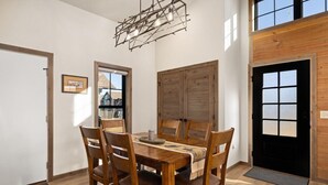 A dining area with a wooden table and chairs, a hanging light fixture, and large windows. - Upscale Mountain Retreat (Red Lodge)