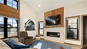 A modern living room with a fireplace, comfortable seating, and a large TV mounted on a wooden wall. - Upscale Mountain Retreat (Red Lodge)