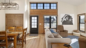 Ein großzügiger Wohnbereich mit hoher Decke, Holzwandverkleidung, einem Esstisch mit Stühlen, einer Couch und einem großen Fenster mit Aussicht.