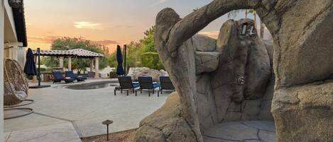 A rock arch over a pool area with lounge chairs and umbrellas.