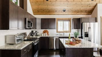 A modern kitchen with dark cabinetry, stainless steel appliances, and a wooden ceiling.