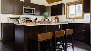A kitchen with dark wood cabinets, a central island with bar stools, a microwave, and a window with blinds.