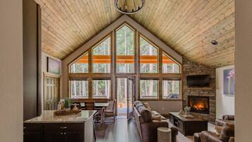 A spacious living area with a high ceiling, large windows, a fireplace, and a cozy seating arrangement.