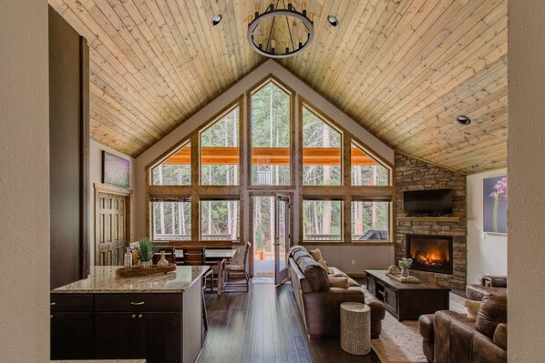 A spacious living area with a high ceiling, large windows, a fireplace, and a cozy seating arrangement.