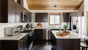 A modern kitchen with dark wood cabinets, stainless steel appliances, a large island, and a wooden ceiling.