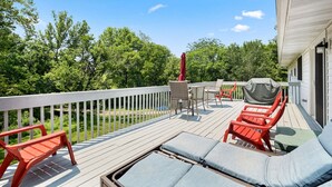 Eine Terrasse mit Gartenmöbeln, darunter rote Stühle und ein Tisch, mit Blick auf ein Gewässer, umgeben von Bäumen.