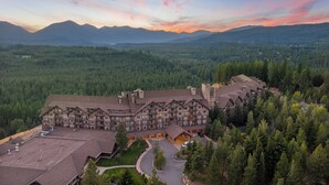 A large lodge with multiple buildings, surrounded by dense forest and mountains in the background.