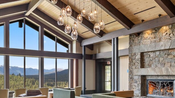 A spacious living area with a stone fireplace, large windows offering mountain views, and modern furniture.