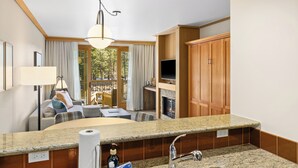 A hotel room with a kitchen area, a seating area with a sofa and chairs, a television, and a fireplace.