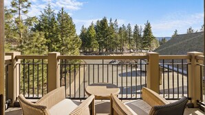 A balcony with wicker furniture and a view of a parking area and trees.