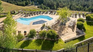A pool area with lounge chairs and a view of a forested mountain range.