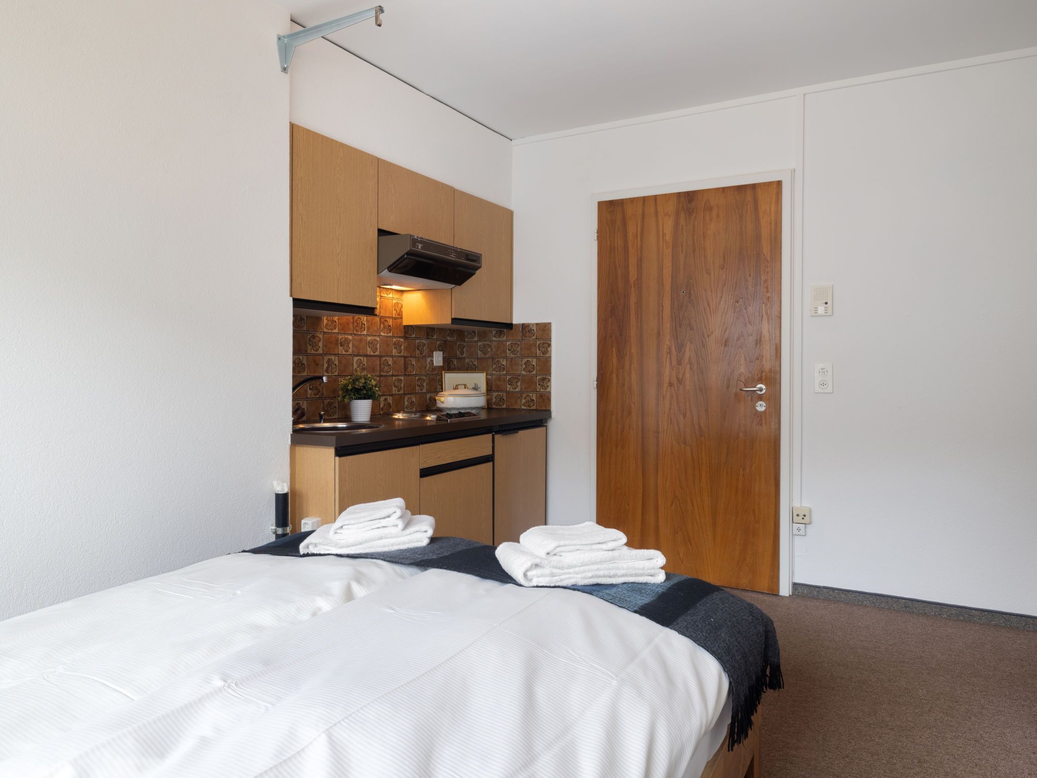Una habitación de hotel pequeña con una cama, una kitchenette y una puerta de madera.